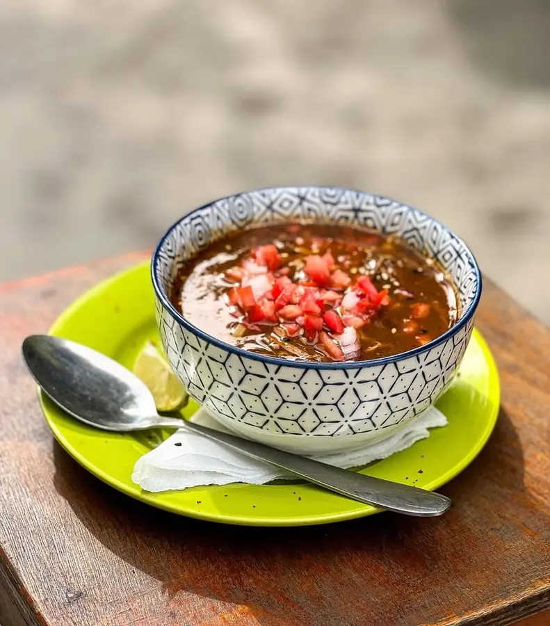 A bowl of birria noodle soup topped with diced tomato