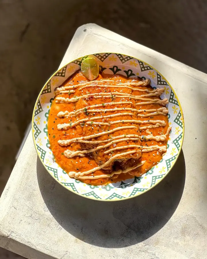 Enchiladas in red sauce with a chipotle drizzle, sesame and lime