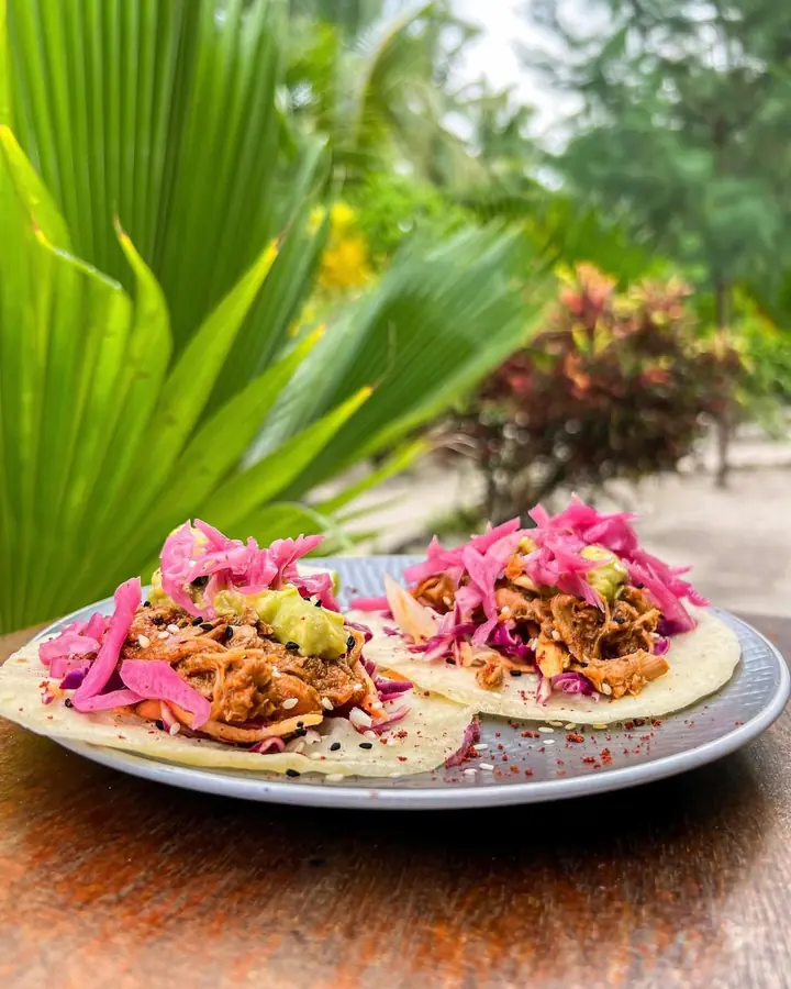 Two tacos topped with pulled meat, pickled red cabbage and guacamole